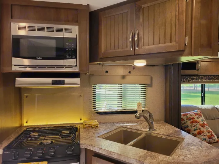 Well-equipped RV rental kitchen featuring a microwave, stove, double sink, ample cabinets, and bright window.. Dutchmen Coleman 2019