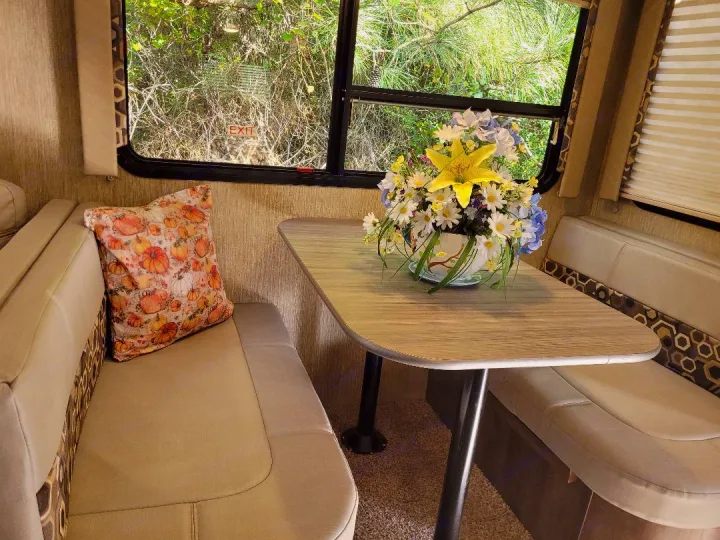 Inviting RV rental interior: a comfy dinette with a pumpkin pillow, vibrant floral centerpiece, and nature outside.. Dutchmen Coleman 2019