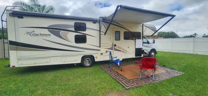 This Coachmen Freelander RV rental is ready for a trip, featuring an extended awning, outdoor mat, and chairs. Ideal for camping.. Forest River Coachmen Freelander 2018