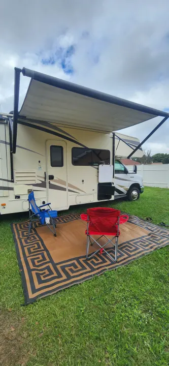 Relax outdoors with this RV rental setup featuring an extended awning, an outdoor rug, and two chairs.. Forest River Coachmen Freelander 2018