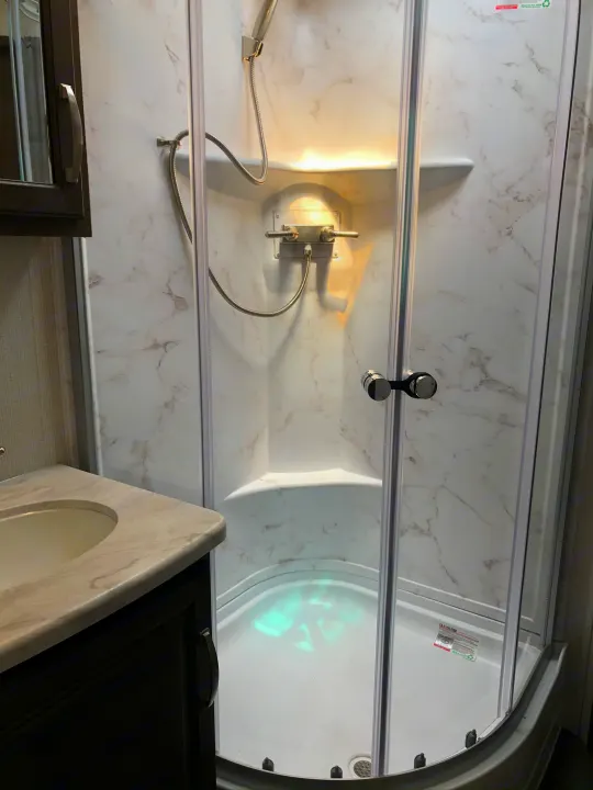 Inside an RV rental: a clean, compact bathroom featuring a corner shower with glass doors and a sink.. Keystone RV Cougar 2021