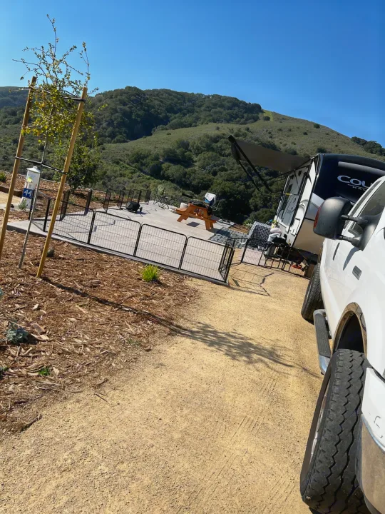 RV rental parked at a scenic campsite (site 44) with patio, fencing, and mountain views under a clear sky. Ideal for camping.. Keystone RV Cougar 2021