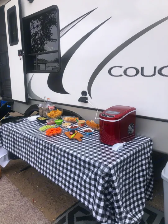 Outdoor RV rental setup with a table full of snacks like chips, veggies, dips, and a red ice maker. Great for camp food!. Keystone RV Cougar 2021