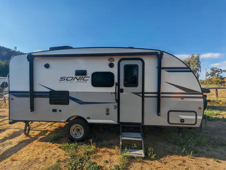 A gray and white Sonic Lite travel trailer, perfect for an RV rental adventure, parked on dry grass under a clear sky.. Sonic Lite 2021