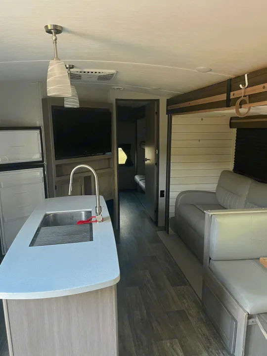 RV rental interior featuring a modern kitchen island with sink, refrigerator, TV, and lounge area.. Crossroads RV Sunset Trail 2022