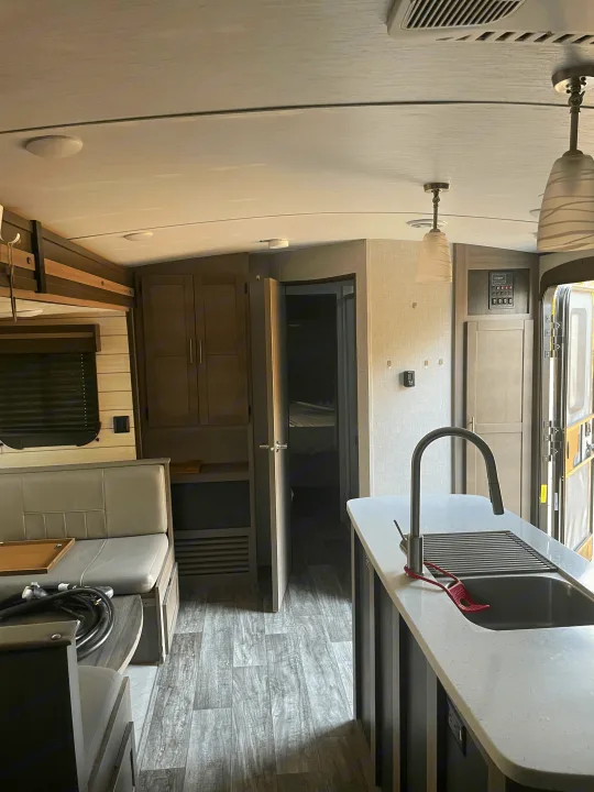 Inside a modern RV rental: a bright living area with dinette seating, kitchen island, and view to the bedroom.. Crossroads RV Sunset Trail 2022