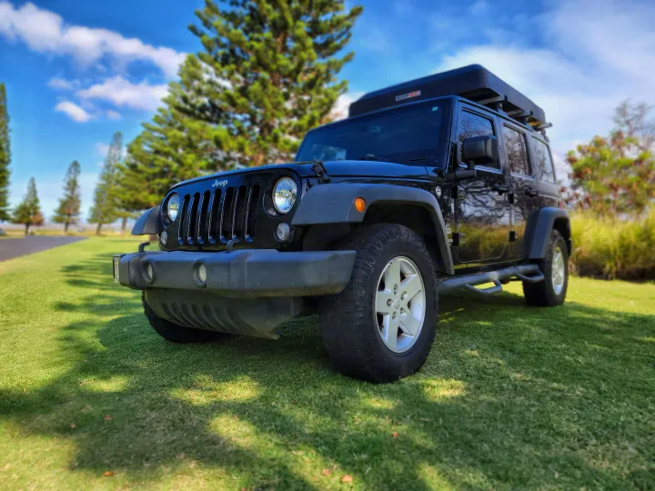 Black Jeep Wrangler with a Roofnest rooftop tent on green grass under a blue sky, ready for your RV rental adventure.. Jeep Jeep Wrangler Overland 2017