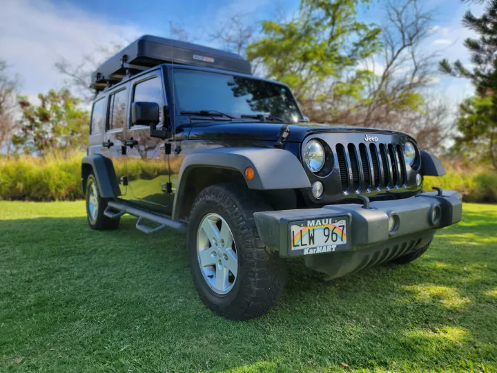 A black Jeep Wrangler with a rooftop tent, parked on green grass. Ideal for your next outdoor rv rental adventure.. Jeep Jeep Wrangler Overland 2017
