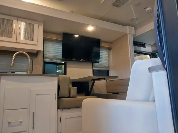 Modern RV rental interior featuring a bright kitchen area with a sink, a dining space with bench seating, and a wall-mounted TV.. 2023