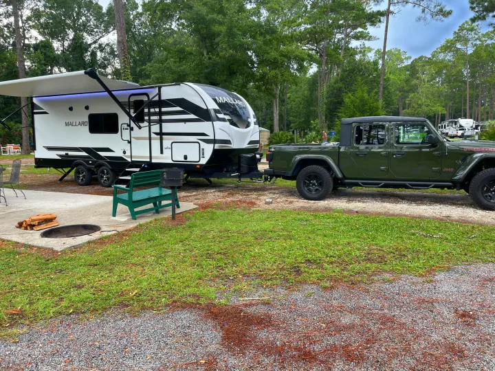 Mallard travel trailer and Jeep Gladiator at a spacious campsite, ready for your next RV rental adventure with a fire pit.. Heartland RVs Mallard 2023