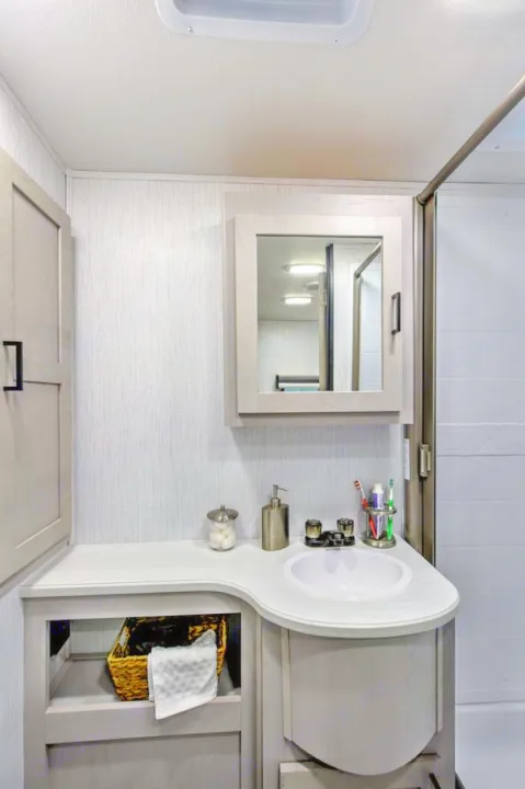 Bright, compact RV bathroom with a wood-toned vanity, white sink, and mirror, perfect for your comfortable RV rental.. Heartland RVs Mallard 2023