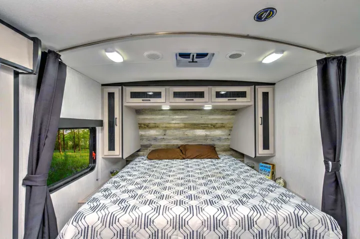 Cozy RV rental bedroom with a full-size bed, overhead cabinets, and a scenic window view.. Heartland RVs Mallard 2023
