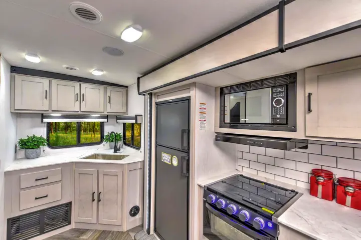 Bright RV rental kitchen showcasing light cabinetry, a corner sink, built-in microwave, stove, and refrigerator.. Heartland RVs Mallard 2023