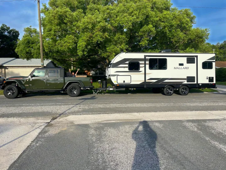 Jeep Gladiator towing a Mallard RV. Two excited people in the truck bed, ready for their RV rental adventure!. Heartland RVs Mallard 2023