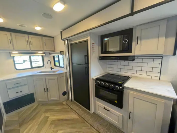 Modern RV rental kitchen with light cabinets, white countertops, black appliances, and subway tile backsplash.. Heartland RVs Mallard 2023