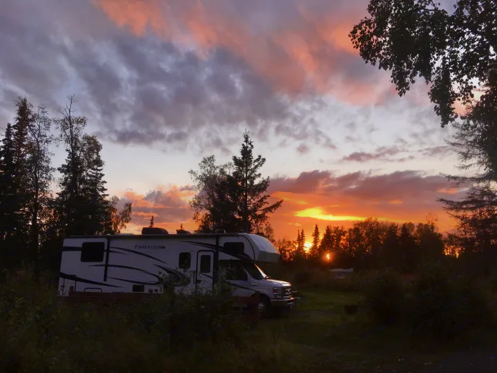 A white Forester RV rental sits in a campsite at sunset, with a vibrant orange and grey sky. Great for nature travel.. Forester LE 2022