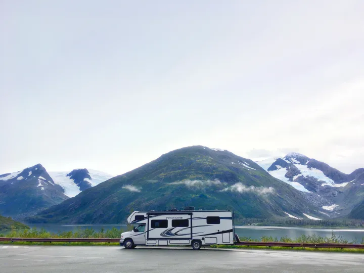 White RV rental parked on a wet road, overlooking a calm lake and majestic mountains with prominent glaciers.. Forester LE 2022