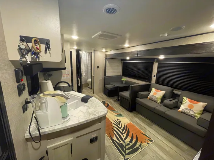 This RV rental interior shows a bright, modern living space with a kitchen, dining booth, and comfy sofa area.. Jayco Jay Flight 2023