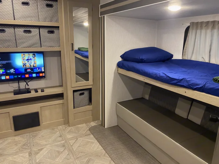 RV rental interior: bunk beds with blue bedding, a convertible seating area, and TV entertainment system.. Forest River Wildwood 2023