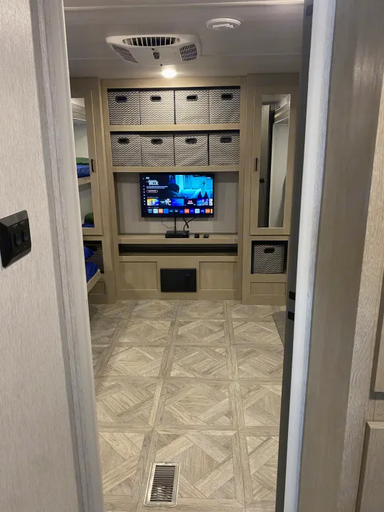 Spacious and modern RV rental interior with entertainment area, chevron storage bins, bunk beds, and AC unit.. Forest River Wildwood 2023