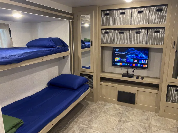 RV rental bunk room: comfy beds, TV, and organized storage shelves. Perfect for family camping trips.. Forest River Wildwood 2023