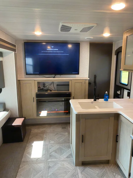 Modern RV rental interior: Smart TV updating, electric fireplace, & kitchen sink area, ready for travel.. Forest River Wildwood 2023