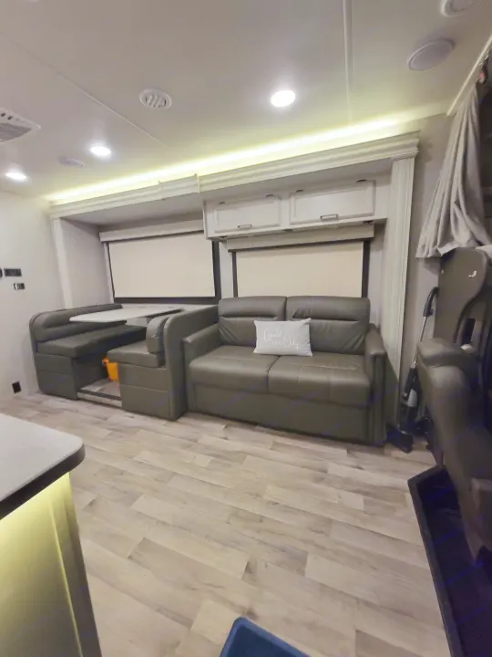 Modern RV rental living space featuring a comfortable sofa, dinette, and light wood-look flooring.. Jayco Greyhawk 2023