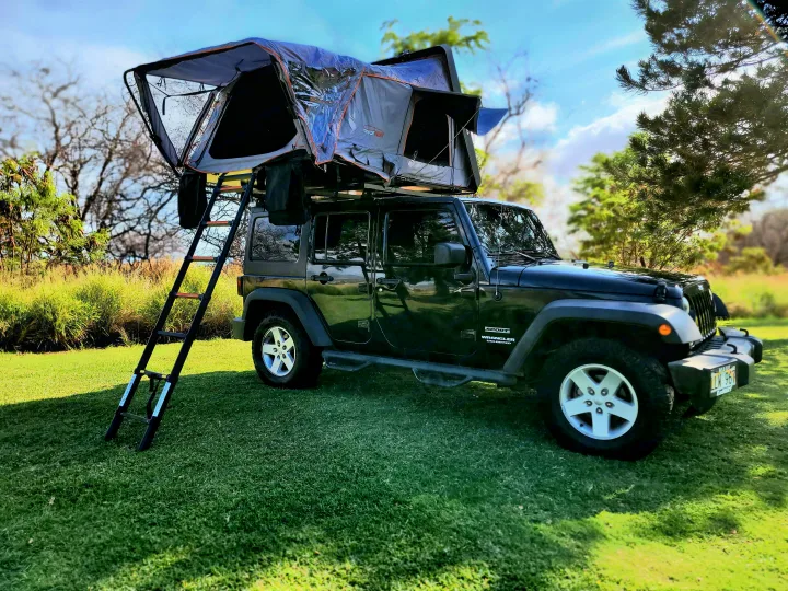 Black Jeep Wrangler with a deployed Roofnest rooftop tent on green grass, ready for your next rv rental adventure.. Jeep Jeep Wrangler Overland 2017