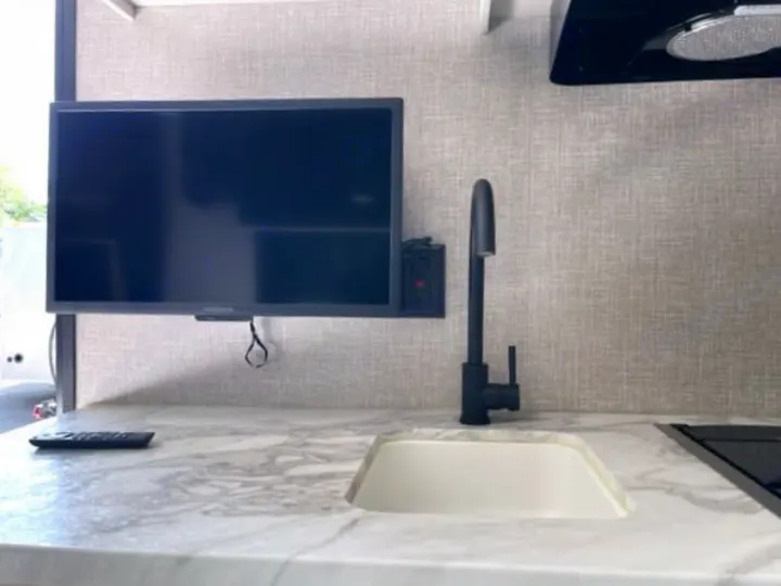 RV rental kitchen: flat-screen TV above a modern sink, black faucet, and sleek marble-look counter.. Jayco Jay Flight 2023