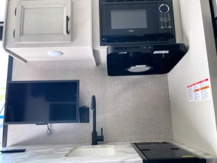 Modern RV rental kitchenette featuring microwave, sink, cooktop, and TV for your next adventure.. Jayco Jay Flight 2023