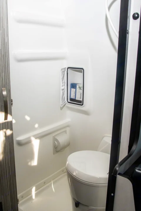 Inside an RV rental: a compact wet bath featuring a toilet, shower, and convenient wall storage with toiletries.. Winnebago Revel 2024