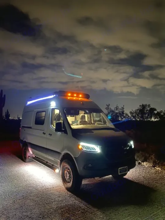 Vibrant RV rental Sprinter van lit up at night on a dirt road.. Winnebago Revel 2024