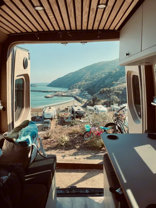 Inside an RV rental, a stunning view of a coastal campground, complete with beach, pier, and lush hills.. Mercedes-Benz Sprinter 2020
