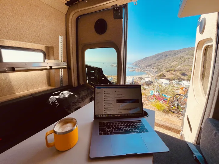 Scenic RV rental setup: remote work with coffee & laptop overlooks a bustling coastal harbor & hills.. Mercedes-Benz Sprinter 2020