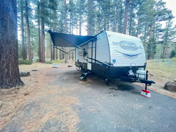 This Springdale RV rental is parked at a serene forested campsite with its awning extended for a relaxing nature escape.. Keystone RV Springdale 2023