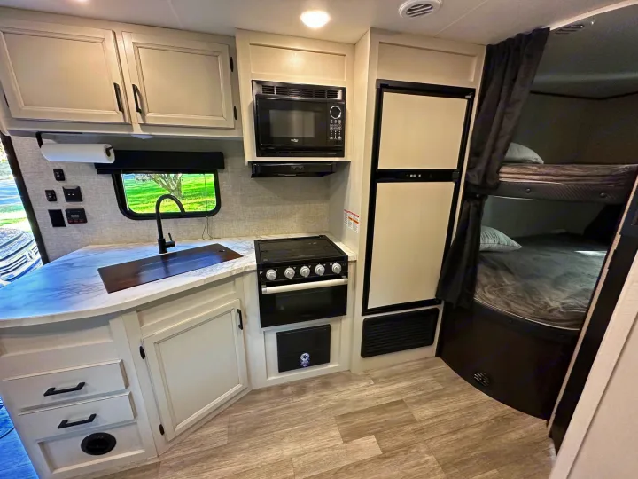 RV rental interior: full kitchen with microwave, stove, sink, and large fridge, plus adjacent bunk beds.. Jayco Jay Flight SLX 2022