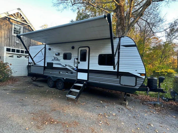 This Jayco travel trailer RV rental with an extended awning is parked next to a rustic barn, surrounded by autumn trees.. Jayco Jay Flight SLX 2022