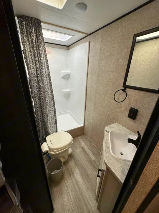 RV rental bathroom with shower, toilet, vanity, sink, mirror, and patterned curtain. Skylight above.. Jayco Jay Flight SLX 2022