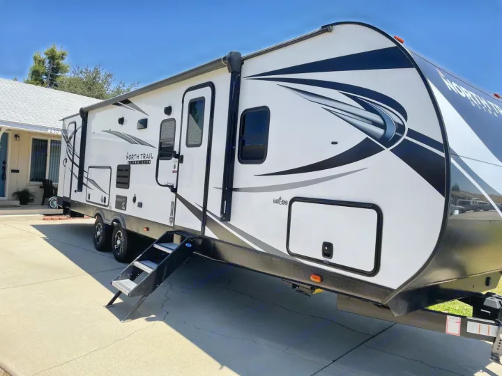 White & black North Trail travel trailer parked on a driveway, ready for your RV rental adventure!. Heartland RVs North Trail 2021