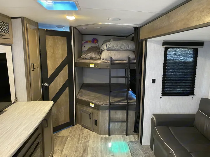 Cozy RV rental interior featuring a bunk bed setup with a ladder, a comfortable sofa, and wood-look flooring.. Heartland RVs North Trail 2021