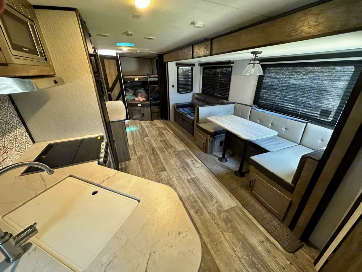 Inside a modern RV rental: A kitchen with sink and stove, dining dinette, sofa, and bunk beds are visible.. Heartland RVs North Trail 2021