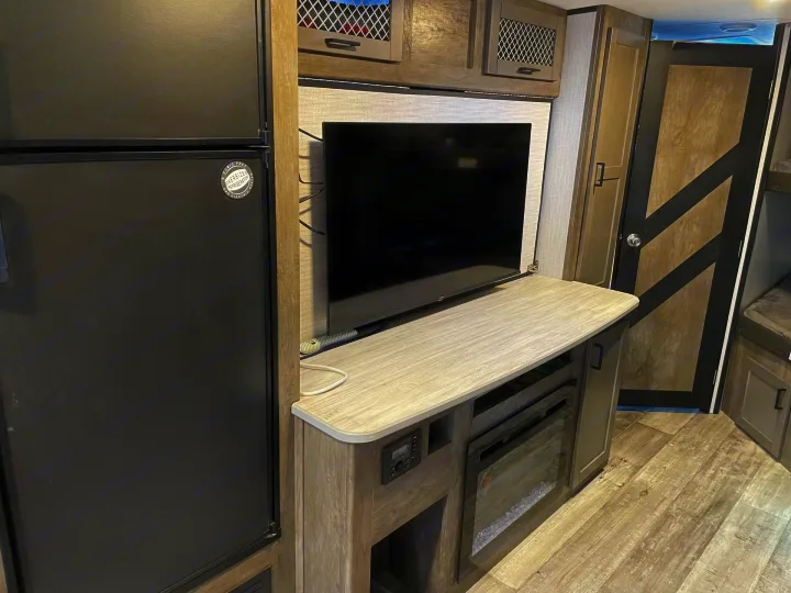 RV rental interior: A modern entertainment unit with TV & fireplace next to a large refrigerator & stylish cabinets.. Heartland RVs North Trail 2021
