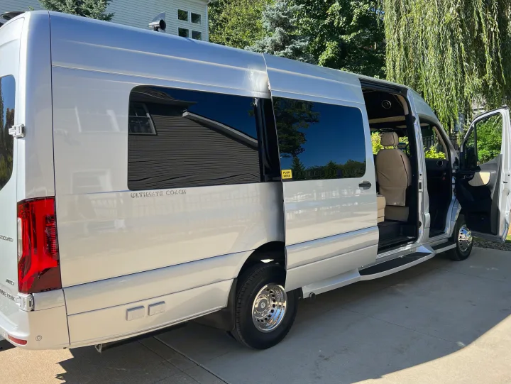 This sleek silver luxury van, ideal for your next rv rental, features an open side door, showcasing its plush interior.. Ultimate Toys Ultimate Coach 2024