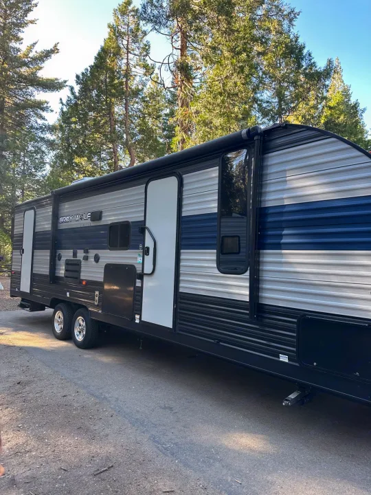 An RV, a Grey Wolf travel trailer, is parked, showcasing its grey, white, and blue striped exterior; ideal for rv rental.. Forest River Cherokee Grey Wolf 2021