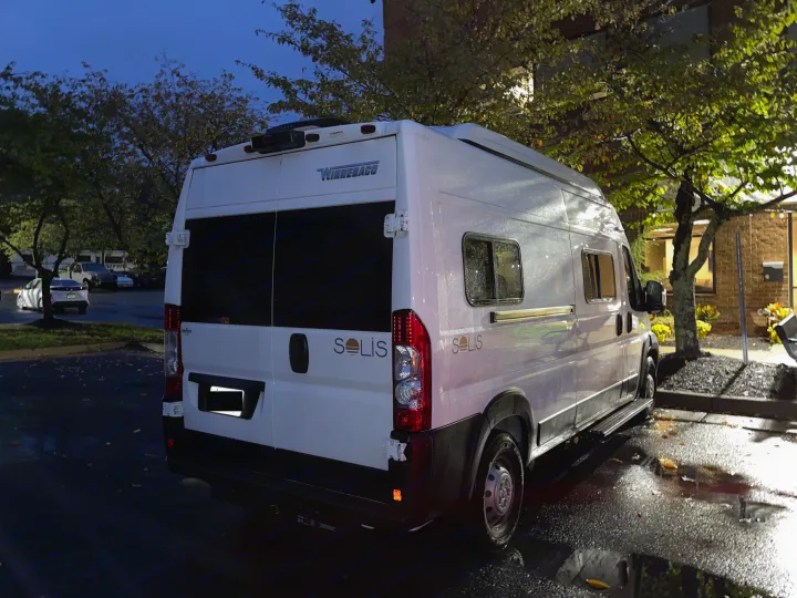 A sleek white Winnebago Solis camper van, perfect for rv rental, parked on wet asphalt at night.. Winnebago Solis 2023