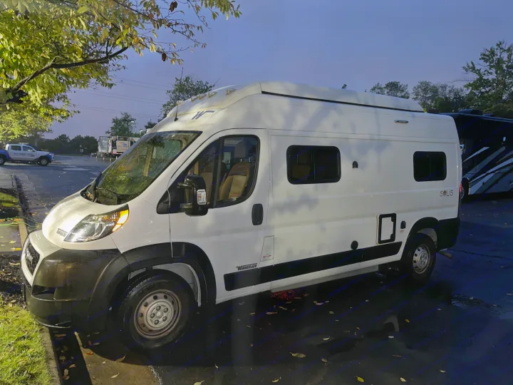 White Winnebago Solis camper van for RV rental, parked on a wet lot at dusk, ready for adventure.. Winnebago Solis 2023