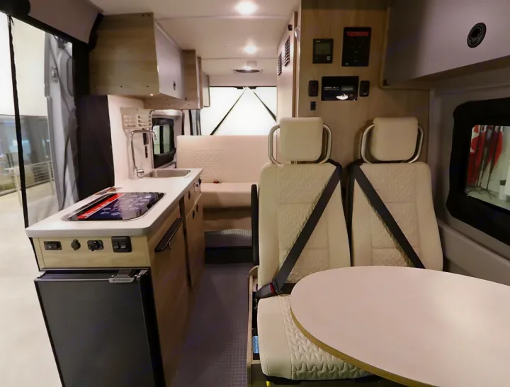 Inside an RV rental, discover a compact kitchen with a sink, stovetop, and fridge, plus versatile seating for travel comfort.. Winnebago Solis 2023