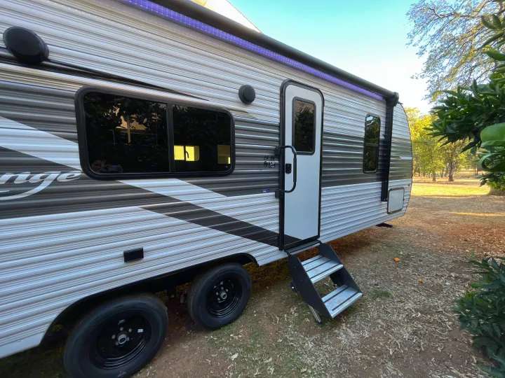 Side view of a modern rv rental parked outdoors, featuring a striped design, door, steps, windows, and awning lights.. Highland Ridge RV Open Range 2023