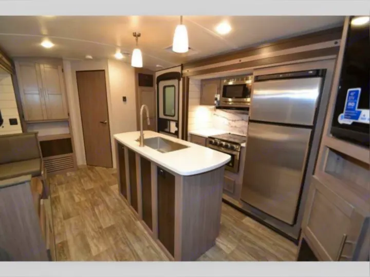 Modern and spacious RV rental interior features a well-equipped kitchen with an island sink, stainless steel appliances, and wood-look flooring.. Crossroads RV Sunset Trail Super Lite 2021