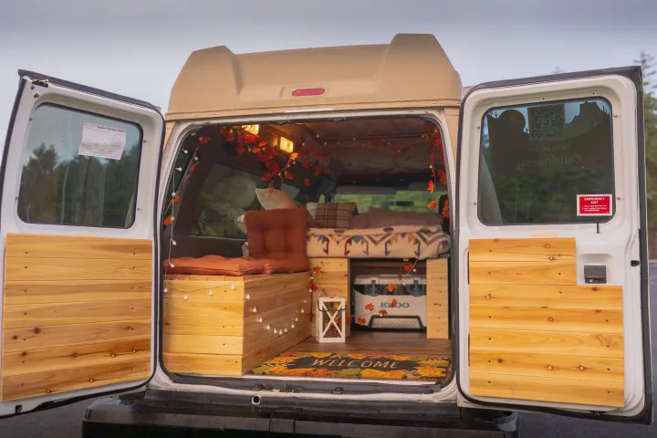 RV rental: View from rear of a cozy campervan with open doors, revealing a fall-decorated interior, bed, and cooler.. Ford Ford E350 2006